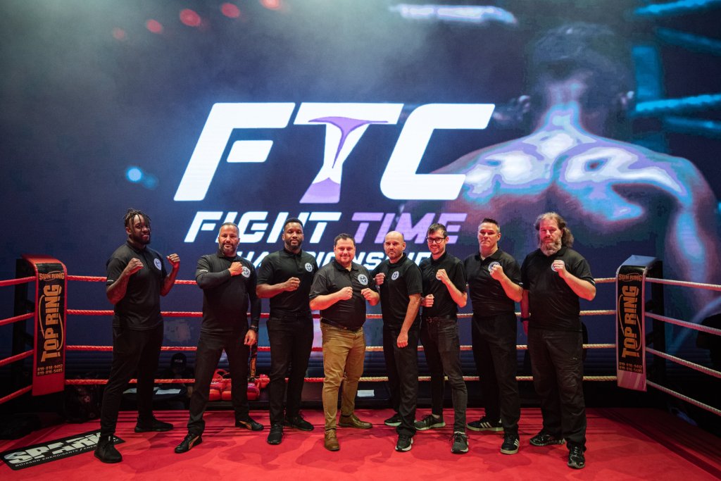 Huit officiels de la WKFQ en polo noir, poings levés, dans le ring d'un gala FTC devant l'écran géant FTC Fight Time Championship